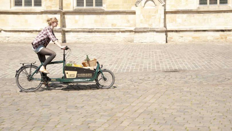 Frau fährt auf einem Lastenrad, welches mit Einkäufen beladen ist