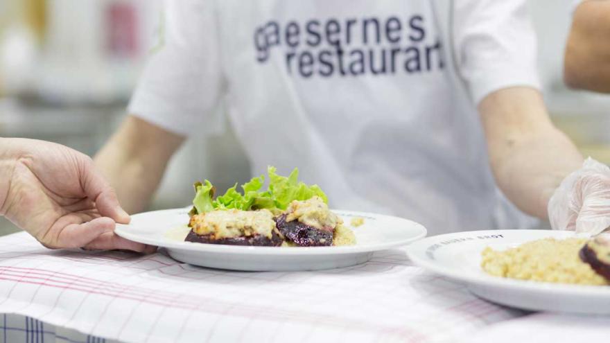 Ein Teller mit Essen, gehalten von einer Person, die ein T-Shirt mit dem Aufdruck "Gläsernes Restaurant" trägt.