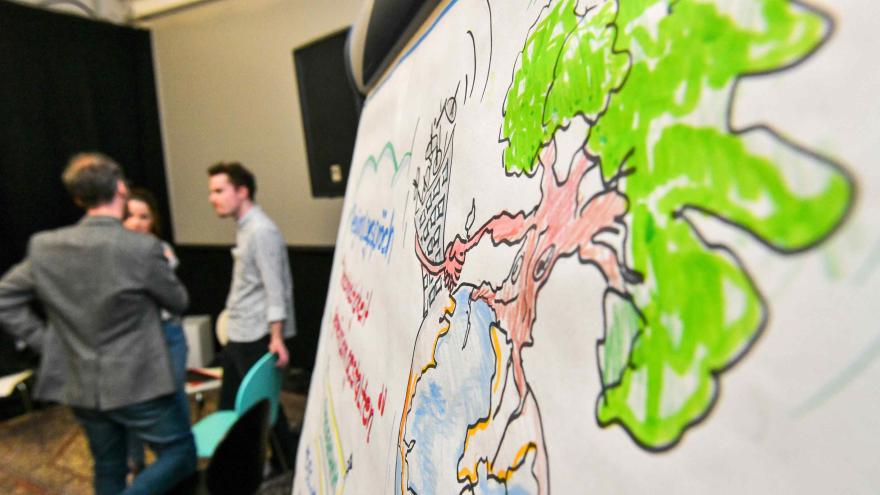 Flipchart mit gemaltem Baum und zwei Personen im Hintergrund