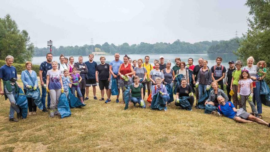 Eine Gruppe Menschen steht mit Müllsäcken auf einer Wiese