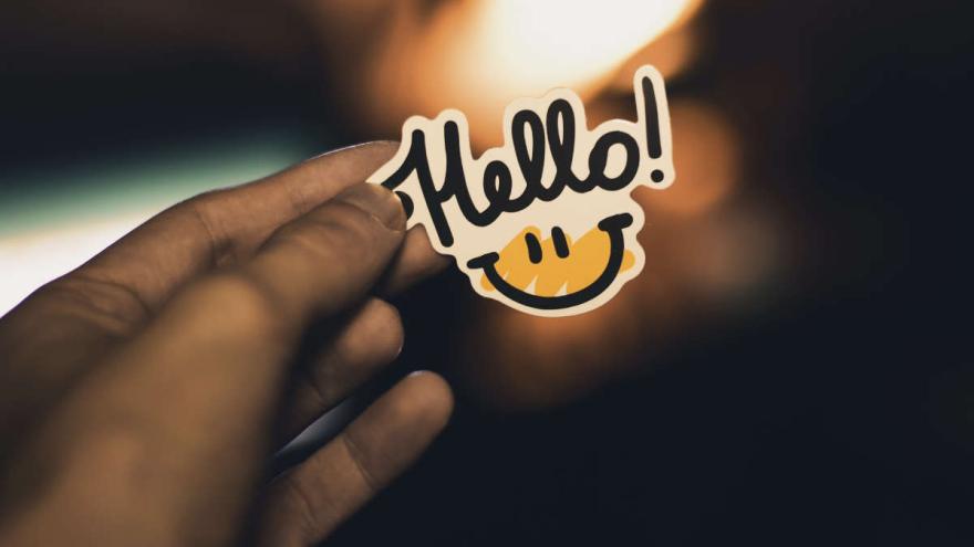Eine Hand hält einen Sticker mit Aufschrift "Hello"