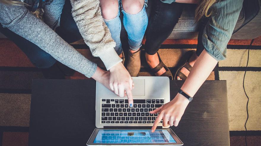 Mehrere Frauen sitzen nebeneinander und zeigen auf den Bildschirm eines Laptops