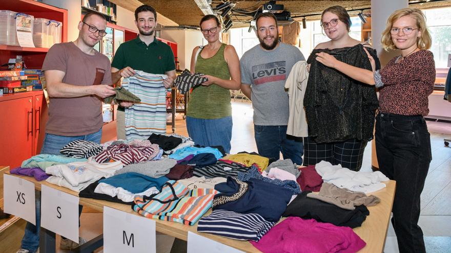 6 Personen stehen nebeneinander hinter Tischen mit Kleidung