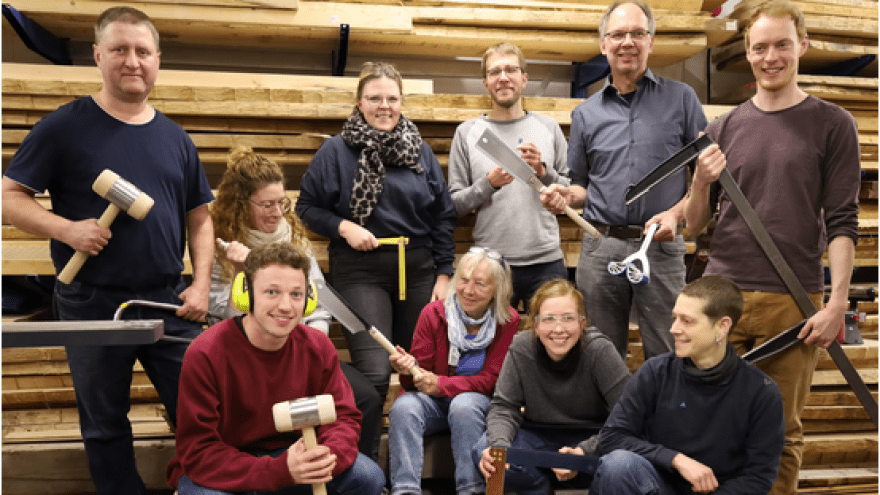 Auf dem Bild sind 10 Personen mit Werkzeugen in einer Holzwerkstatt zu sehen.