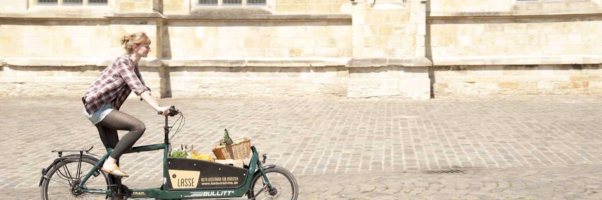 Frau fährt auf einem Lastenrad, welches mit Einkäufen beladen ist