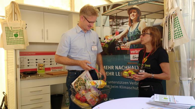 Zwei Leute unterhalten sich am Stand von MehrWert NRW und halten Obst-/Einkaufskörbe