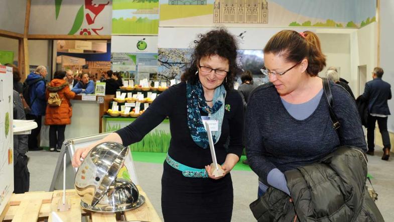 Zwei Frauen sehen nach, was sich unter den Servierglocken am MehrWert-Stand befindet.