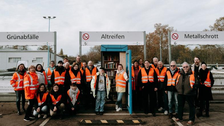 Gruppenfoto vor dem Bücherschrank, der auf dem Gelände des Recyclinghofs steht