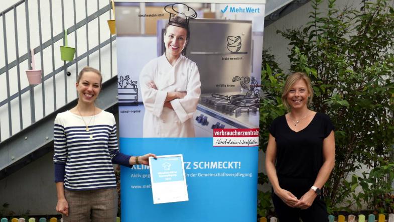 Kita-Leiterin Christine Lauck (r.) nimmt die Urkunde im Außenbereich der Kita entgegen.