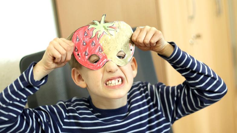 Ein Junge hält eine selbstbemalte Maske vor sein Gesicht