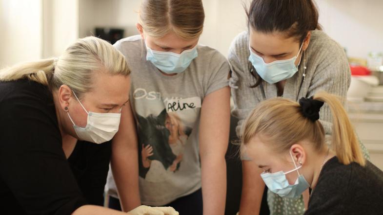 Mehrere Kinder und eine Erwachsene betrachten etwas auf einem Tisch 