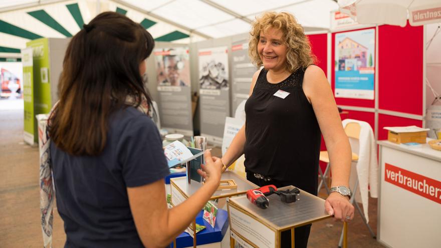 Zwei Frauen sprechen vor Ausstellungswänden in einem Zelt miteinander