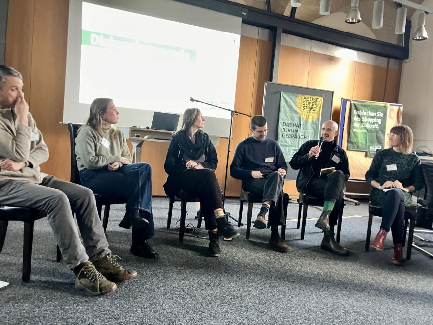 Sechs Personen sitzen auf Stülen und diskutieren in einer Podiumsdiskussion