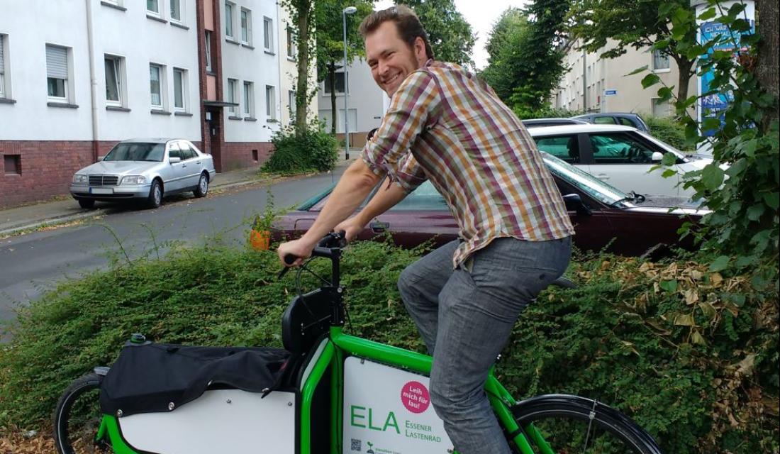 Ein Mann fährt auf einem grünen Lastenrad, auf dem ELA steht.