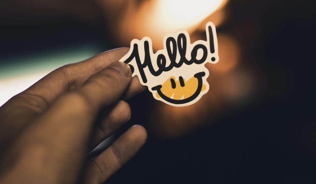 Eine Hand hält einen Sticker mit Aufschrift "Hello"