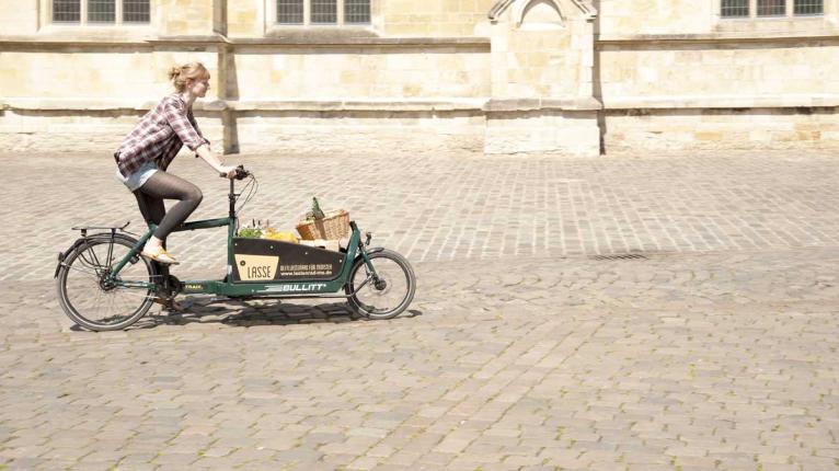 Frau fährt auf einem Lastenrad, welches mit Einkäufen beladen ist